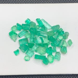 Könnte beinhalten: Eine Ansammlung kleiner, roher Smaragd-Edelsteine in verschiedenen Schattierungen von lebhaftem Grün. Die Steine weisen unregelmäßige, gezackte Formen mit durchscheinenden und undurchsichtigen Texturen auf und zeigen natürliche kristalline Strukturen.