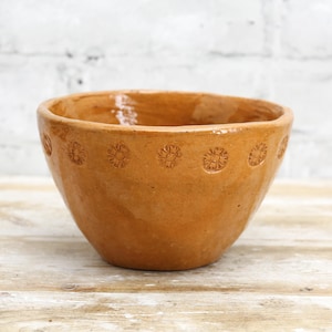 May include: A terracotta bowl with a decorative design of small circles around the rim. The bowl is a light brown colour and has a smooth, slightly textured surface.