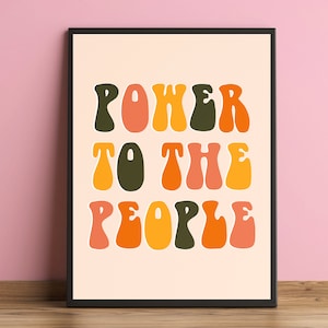 May include: A framed print with the text "POWER TO THE PEOPLE" in a retro, colourful font. The letters are in shades of orange, yellow, green, and pink.