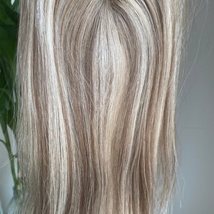 May include: A light blonde human hair topper with a lace base. The hair is straight and has a natural look.