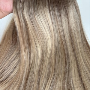 Peut inclure: Gros plan sur une extension de cheveux brun clair et blond. Les cheveux sont lisses et droits, avec un effet ombré subtil.