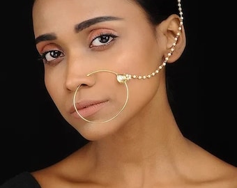 May include: A gold nose ring with a pearl and chain attached to the ear. The nose ring is a simple hoop design.