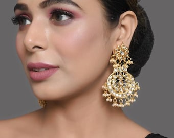 May include: A pair of gold earrings with white pearl accents and a floral design. The earrings are dangling and have a circular shape.