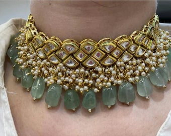 Op de afbeelding: Een gouden en groene choker ketting met een groot, versierd middelstuk en hangende groene stenen.