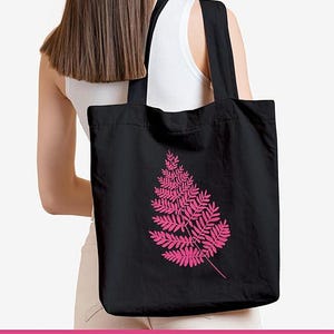 May include: A black cotton canvas tote bag with a pink fern design. The bag has long straps and is made of reusable material.  Cotton Canvas Eco-Friendly Reusable Totebag