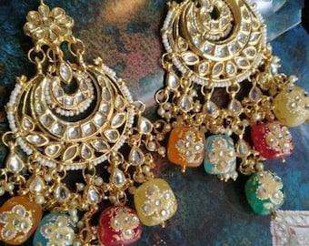 May include: A pair of gold-toned chandelier earrings. Each earring features a floral top, a crescent-shaped design with clear stones, and dangling colorful beads in orange, yellow, red, green, and blue. Small white beads are also incorporated.
