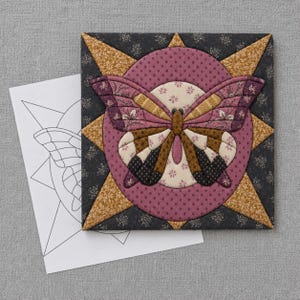 Könnte beinhalten: Ein quadratischer Stoff-Quiltblock mit einer zentralen Schmetterlingsapplikation in Mauve-, Braun- und Cremetönen. Der Schmetterling ist vor einem kreisförmigen mauvefarbenen Hintergrund mit einem sternförmigen Rand aus senfgelbem und dunkelgrauem Blumenstoff platziert.