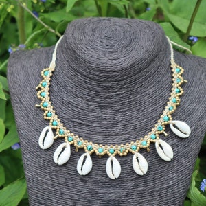 May include: A white shell necklace with turquoise and gold beads. The necklace is on a gray mannequin bust.