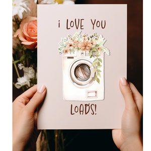 May include: A white card with a watercolor illustration of a washing machine with flowers on top. The card says "i love you loads!"