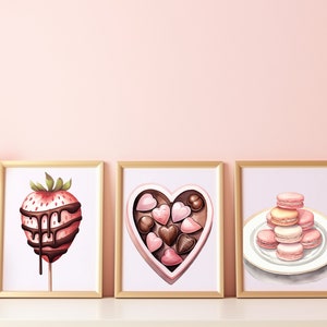 May include: Three framed illustrations of Valentine's Day treats. The first shows a chocolate-covered strawberry on a stick. The second shows a heart-shaped box of chocolates. The third shows a stack of pink and white macarons on a white plate.