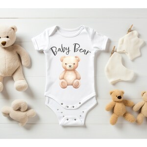 May include: White baby onesie with a brown teddy bear illustration and the text "Baby Bear".