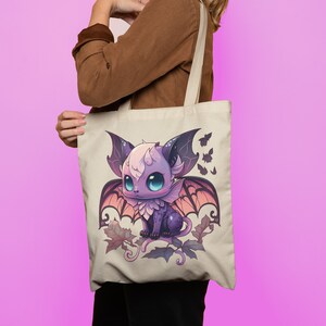 May include: A beige tote bag featuring a purple and pink bat illustration. The bat has large wings and is surrounded by smaller bats. The bag has a brown strap.