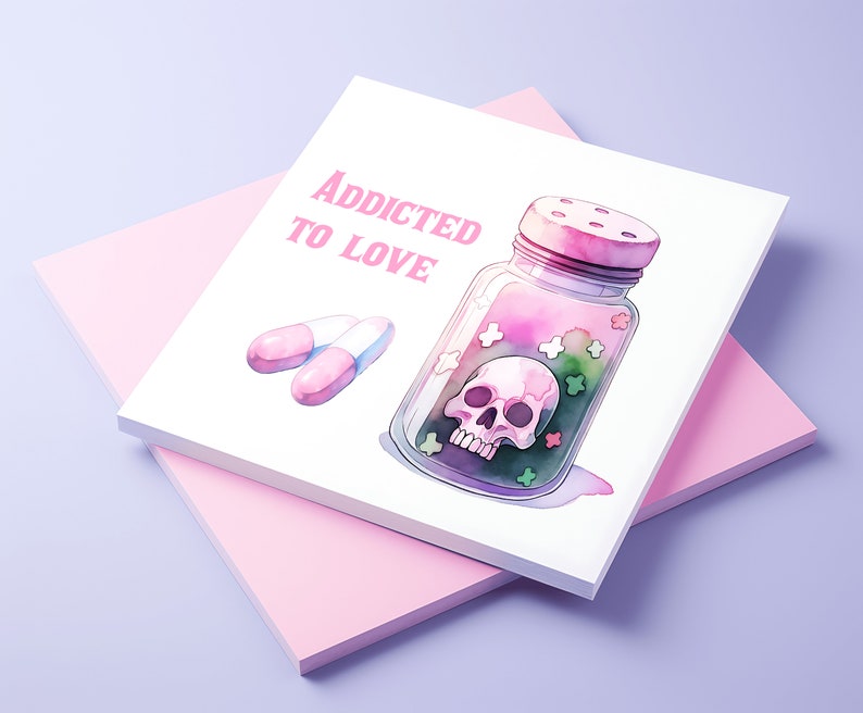 Puede incluir: Una tarjeta blanca con el texto "Addicted to Love" en letras rosas. Un frasco de vidrio con una tapa rosa y una calavera en su interior est&aacute; lleno de caramelos rosas, verdes y blancos. Dos pastillas rosas est&aacute;n sobre la tarjeta.