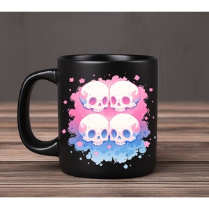 Puede incluir: Taza de cer&aacute;mica negra con un dise&ntilde;o de cuatro calaveras rosas y azules con llamas sobre un fondo de nube rosa y azul.