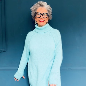 Könnte beinhalten: Ein hellblauer, übergroßer Rollkragenpullover mit langen Ärmeln und einer lockeren Passform. Der Pullover ist aus einem weichen, flauschigen Material gefertigt.
