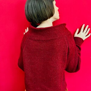 May include: A maroon knitted jumper with a high neckline and long sleeves. The jumper is made of a soft, textured yarn.