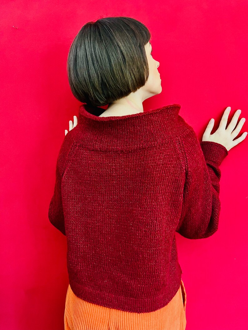May include: A maroon knitted jumper with a high neckline and long sleeves. The jumper is made of a soft, textured yarn.