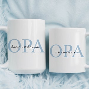Könnte beinhalten: Zwei weiße Keramikbecher mit blauer Beschriftung, die "OPA" lautet, mit den Namen "David & Hanna" und "Leonie" darunter.