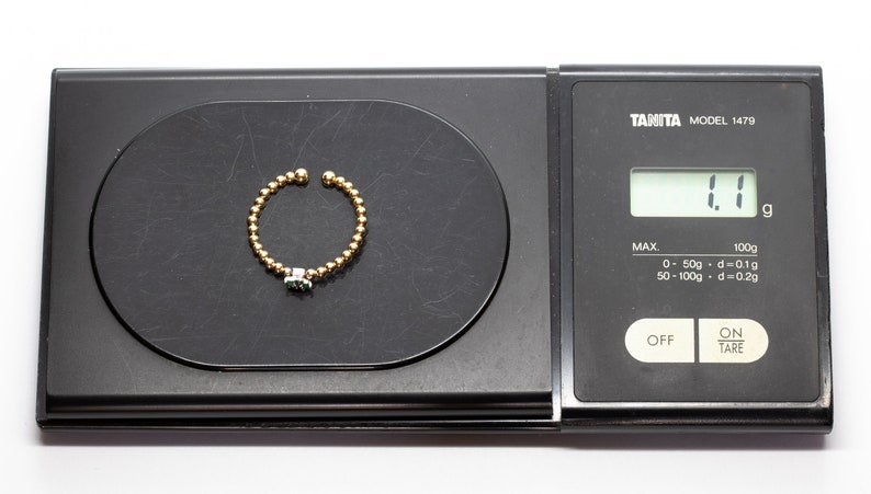 Puede incluir: Un anillo de oro con una piedra verde en una b&aacute;scula digital que marca 1,1 gramos.