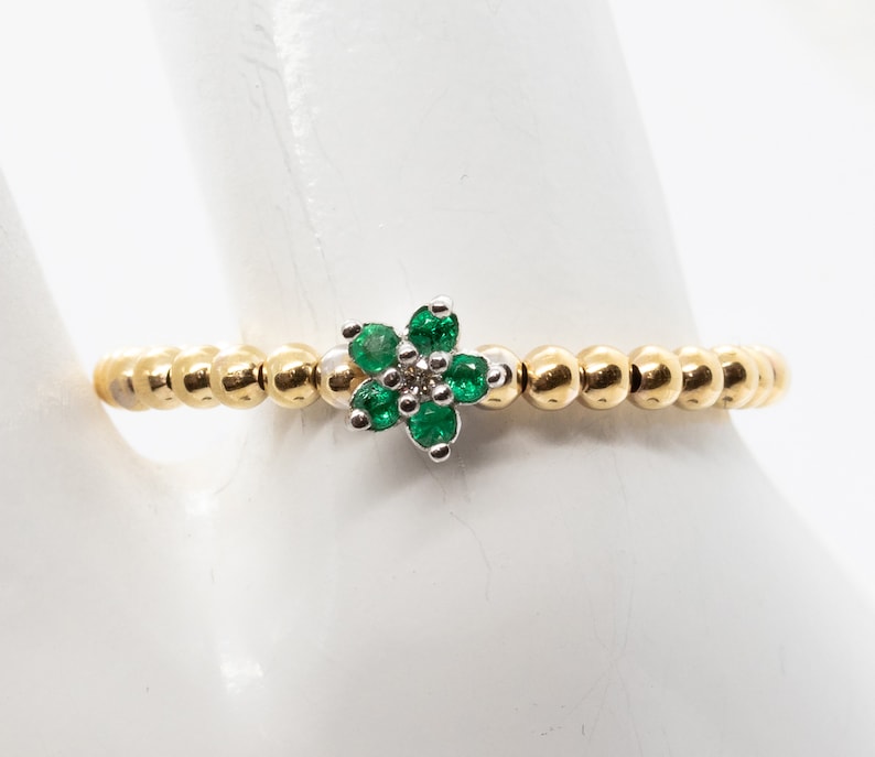 Puede incluir: Un anillo de oro con un dise&ntilde;o en forma de flor con piedras preciosas verdes y un peque&ntilde;o diamante en el centro.