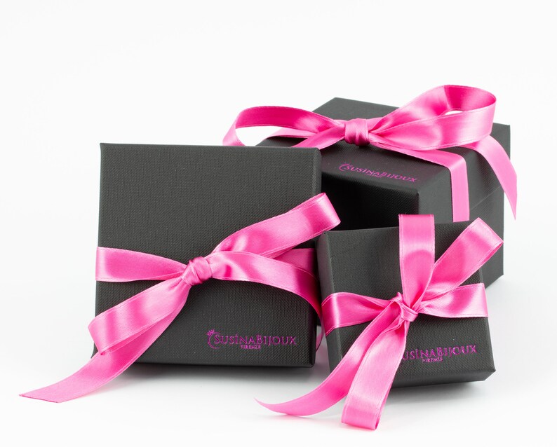 Puede incluir: Tres cajas de regalo negras con lazos de cinta de sat&eacute;n rosa. Las cajas est&aacute;n apiladas una encima de la otra. La caja superior tiene el texto "CusinaBijoux" impreso.