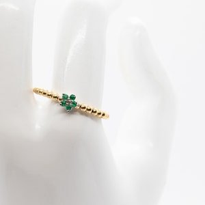 Puede incluir: Un anillo de oro con un peque&ntilde;o dise&ntilde;o de flor verde. El anillo est&aacute; hecho de peque&ntilde;as cuentas doradas.