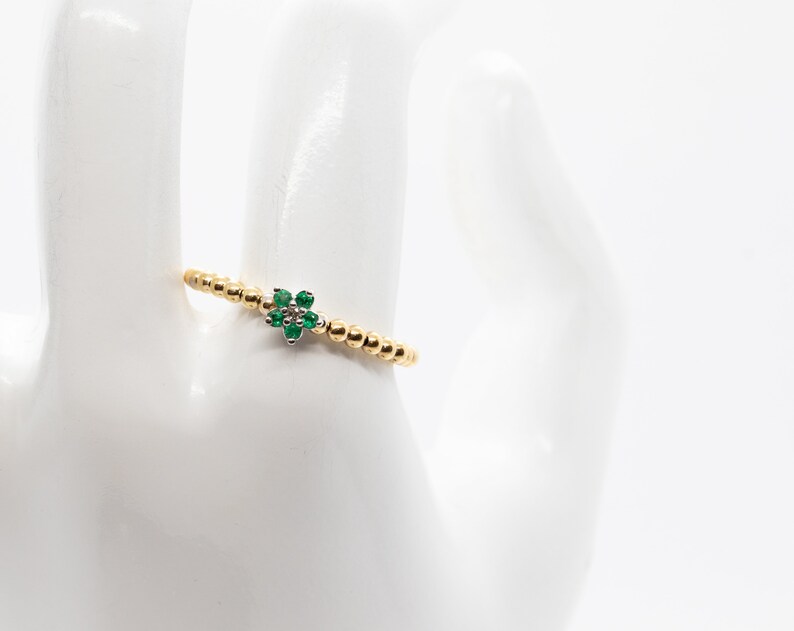 Puede incluir: Un anillo de oro con un peque&ntilde;o dise&ntilde;o de flor verde. El anillo est&aacute; hecho de peque&ntilde;as cuentas doradas.