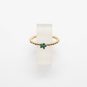 Puede incluir: Un anillo de oro con un peque&ntilde;o dise&ntilde;o de flor verde. La flor tiene una piedra central y est&aacute; rodeada de piedras verdes m&aacute;s peque&ntilde;as.