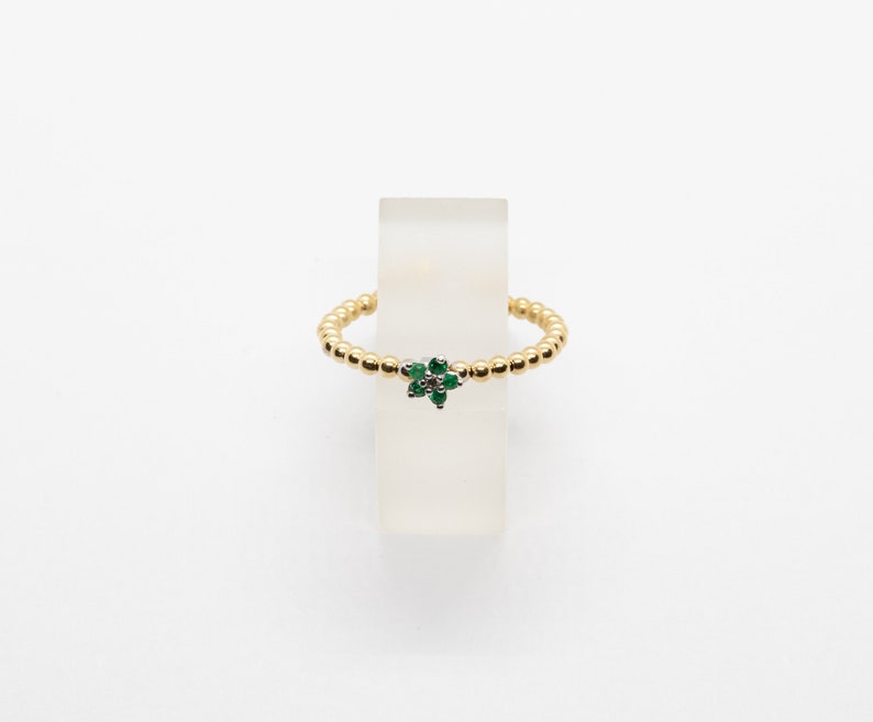 Puede incluir: Un anillo de oro con un peque&ntilde;o dise&ntilde;o de flor verde. La flor tiene una piedra central y est&aacute; rodeada de piedras verdes m&aacute;s peque&ntilde;as.
