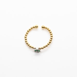 Puede incluir: Un anillo de cuentas doradas con un peque&ntilde;o dije de piedra verde y blanca.