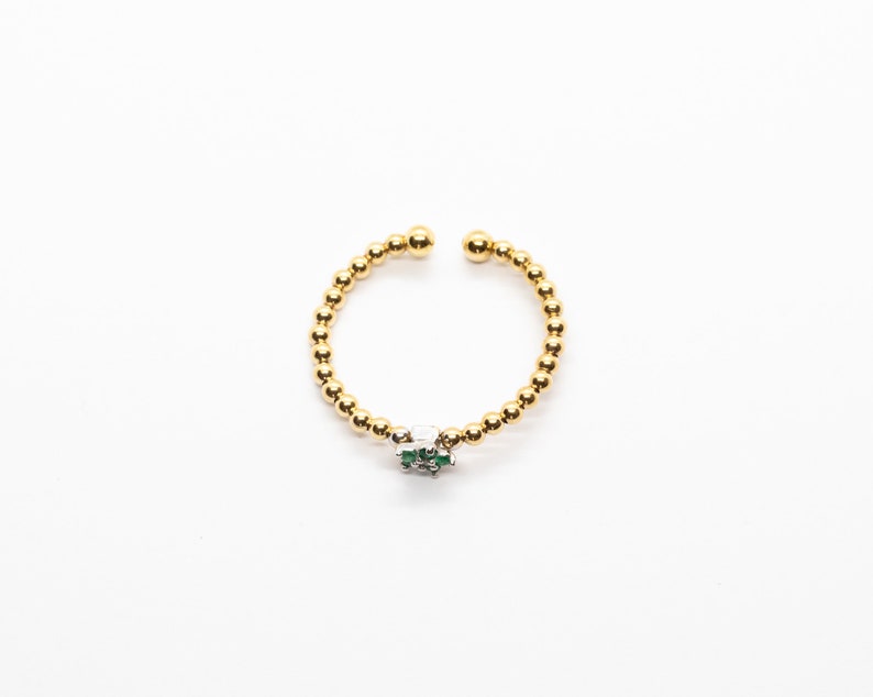 Puede incluir: Un anillo de cuentas doradas con un peque&ntilde;o dije de piedra verde y blanca.