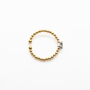 Puede incluir: Un anillo de oro con una peque&ntilde;a piedra preciosa verde engastada en un engaste de plata. El anillo est&aacute; hecho de peque&ntilde;as cuentas doradas.