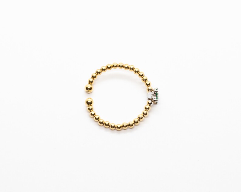 Puede incluir: Un anillo de oro con una peque&ntilde;a piedra preciosa verde engastada en un engaste de plata. El anillo est&aacute; hecho de peque&ntilde;as cuentas doradas.
