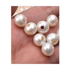 May include: A close-up of a hand holding a group of white pearl beads with holes in the center. The beads are smooth and glossy.