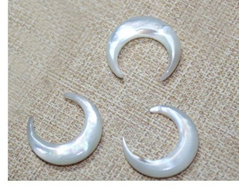 May include: Three iridescent, crescent-shaped pendants. The pendants have a pearlescent sheen and a curved design. They are arranged on a neutral, textured background. The pendants are likely for jewelry making or crafting.
