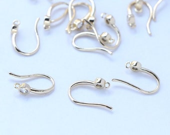 May include: A group of gold-toned earring hooks with a clear crystal bead at the top of each hook.