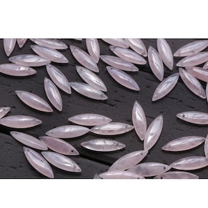 May include: A collection of pale pink, oval-shaped gemstone beads. The beads are smooth and polished, with a subtle shimmer.