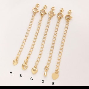 May include: Five gold extender chains with different charms. The charms include a heart, a small heart, a teardrop, and a larger heart. The chains are all the same length and have a lobster clasp.