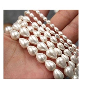 May include: A strand of white pearlescent teardrop beads of varying sizes. The beads are strung on a clear thread and are arranged in a graduated pattern.