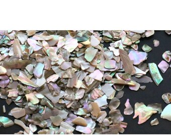 Puede incluir: Un montón de piezas de concha de nácar de forma irregular, iridiscentes y multicolores. Las piezas de concha están esparcidas sobre una superficie negra.