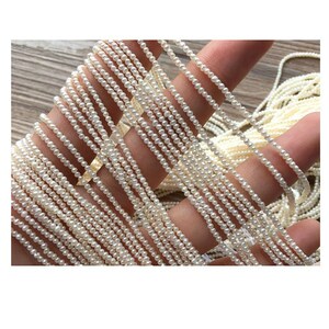 May include: A strand of white freshwater pearls, strung on a thin thread. The pearls are small and uniform in size, creating a delicate and elegant look.