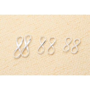 Może przedstawiać: Trzy zestawy srebrnych zawieszek w kształcie nieskończoności w różnych rozmiarach. Zawieszki są gładkie, skręcone i fakturowane.