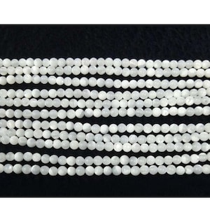 Op de afbeelding: Een streng witte ronde kralen gemaakt van parelmoer. De kralen zijn glad en hebben een lichte iriserende glans.