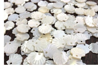 May include: A large group of white seashell-shaped buttons with two holes each. The buttons are arranged in a random pattern on a wooden surface.