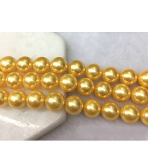 Puede incluir: Una hebra de cuentas de perlas de color amarillo dorado. Las perlas son redondas y lisas, y tienen un alto brillo.