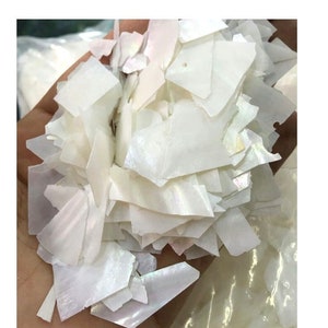 May include: A pile of white iridescent mother of pearl shell flakes. The flakes are various sizes and shapes.