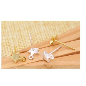 Könnte beinhalten: Drei goldene und silberne sternförmige Ohrring-Findings mit Sprungringen. Die Findings befinden sich auf einer Holzoberfläche.