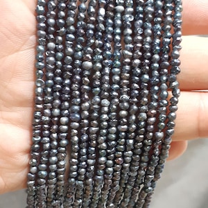 Puede incluir: Una hebra de perlas de agua dulce gris oscuro, cada perla es ligeramente irregular en forma y tiene un sutil brillo iridiscente.