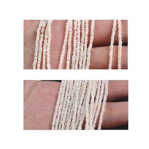 May include: Close-up of multiple strands of small, white pearls. The pearls are strung together, creating a delicate and elegant appearance. The strands are held in a hand, showcasing the texture and colour of the pearls.