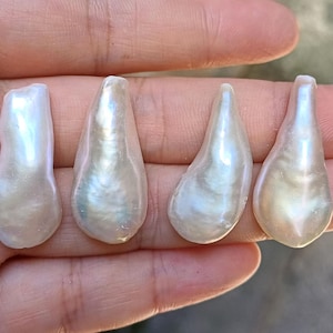 Puede incluir: Cuatro perlas iridiscentes en forma de lágrima, con un brillo blanco nacarado. Las perlas varían ligeramente en forma y tamaño, cada una mostrando texturas naturales únicas y sutiles variaciones de color. Ideales para joyería.